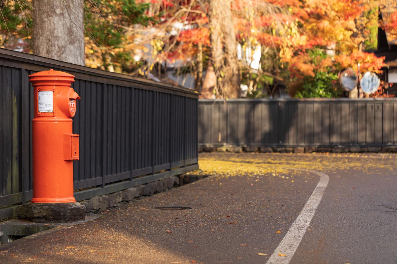 秋の紅葉した落ち葉が散る武家屋敷の路地に立つ赤い郵便ポスト