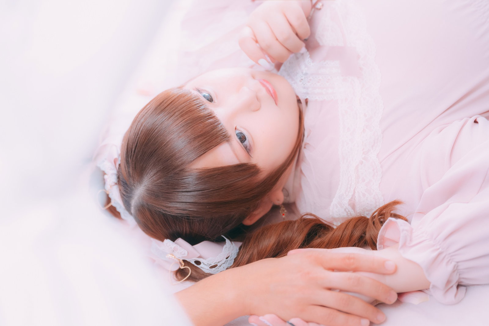 ピンク系の布団で彼の手を握りしめながら寝転ぶ女性［モデル：あづき］