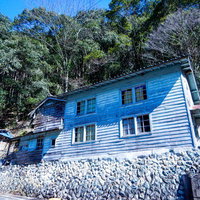 石垣の上に立つボロボロの古民家（廃屋）周囲の森林風景の写真