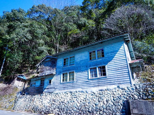 石垣の上に立つボロボロの古民家（廃屋）周囲の森林風景