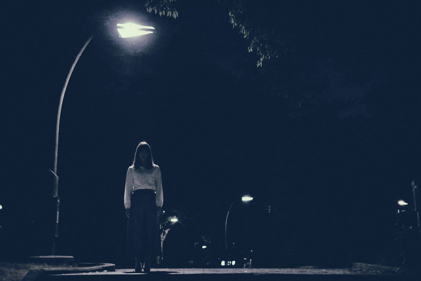 夜道の街灯の下でこちらを見つめる女性［モデル：さとうゆい］