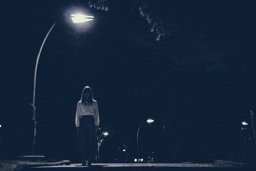 街灯の下からこちらを見つめる女性のホラー