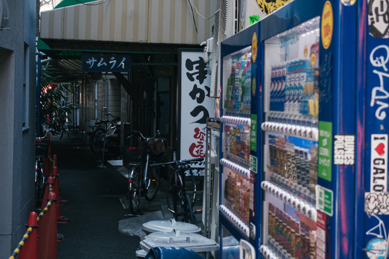 狭い路地裏に青い自動販売機と看板が設置された住宅街の風景
