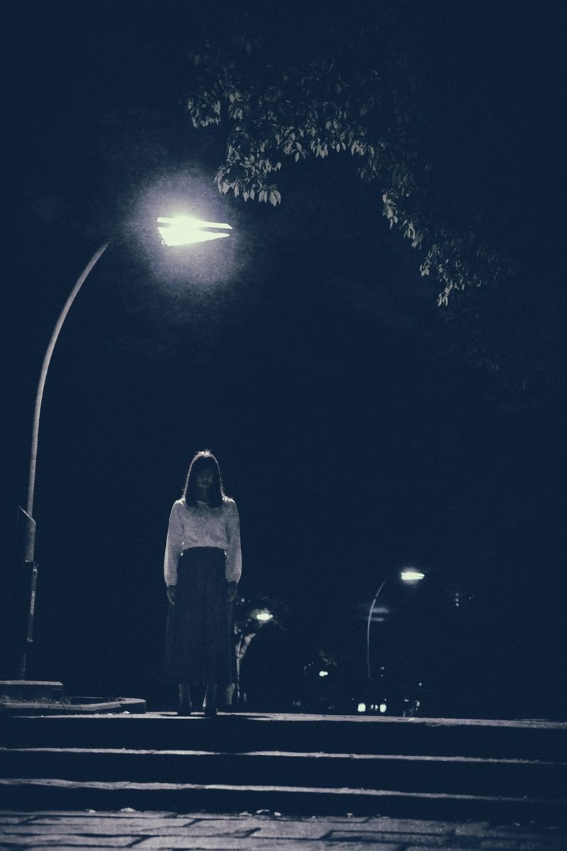 暗い夜道で街灯の下に立つ女性のシルエット［モデル：さとうゆい］