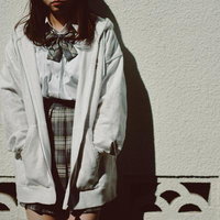 白いパーカーを羽織った制服姿でタイルの塀によりかかるJKの写真