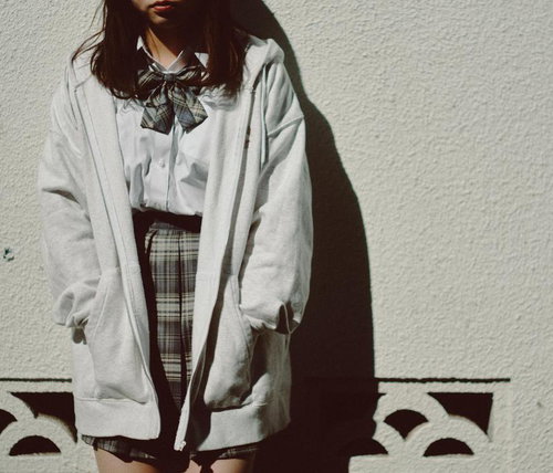 白いパーカーを羽織った制服姿でタイルの塀によりかかるJK