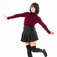 エンジ色のニットを着て両手を広げて片足立ちする女性の写真