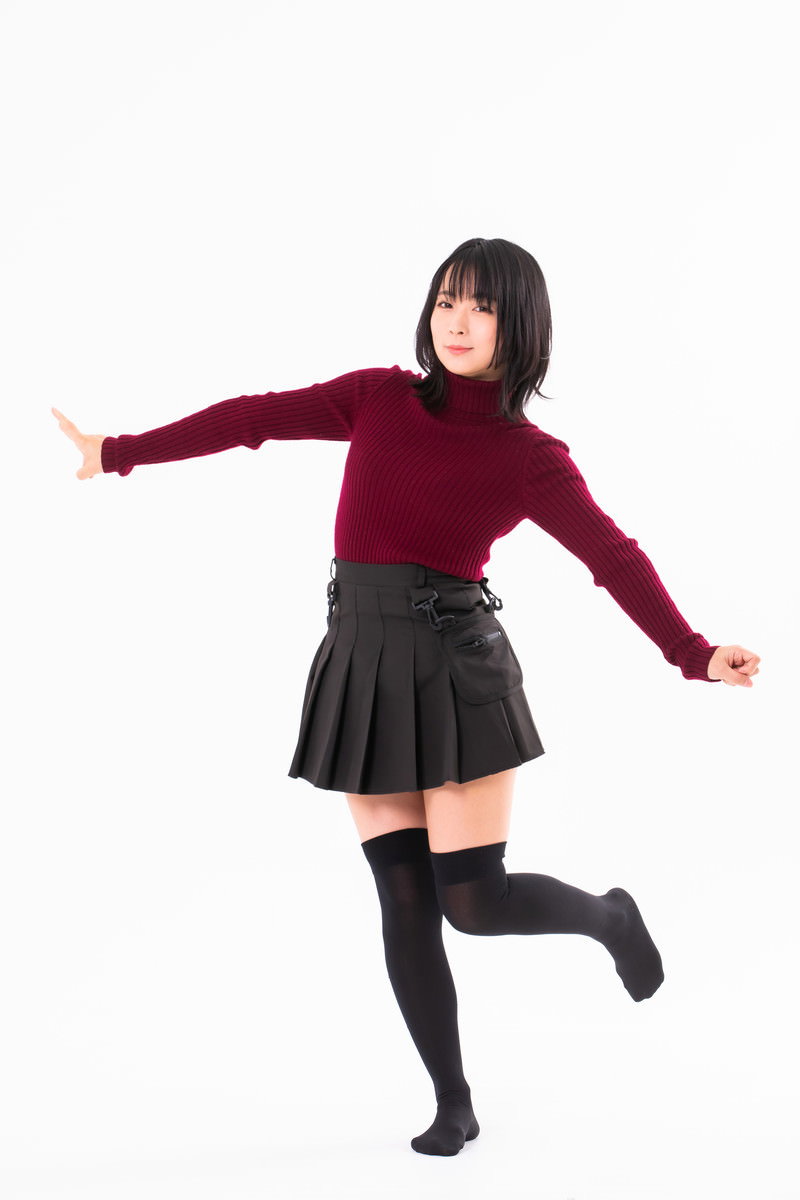 エンジ色のニットとプリーツスカート、黒いハイソックスを履いて両手を広げながら片足立ちする女性［モデル：にゃるる］