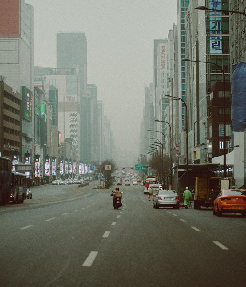 スモッグがかかった韓国の幹線道路。両側にビル群が立ち並び、複数の車両が走行している。