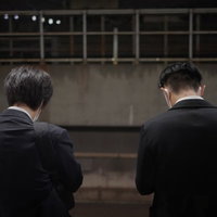 電車を待つサラリーマンの後ろ姿、仕事帰りのホームで待機する通勤風景の写真