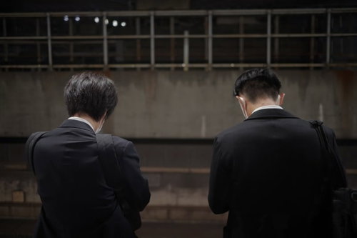 電車を待つサラリーマンの後ろ姿、仕事帰りのホームで待機する通勤風景