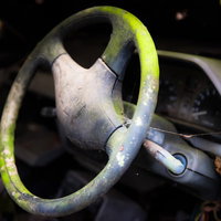 朽ちた車のハンドル、変色した緑色に浮かぶサビと汚れの写真