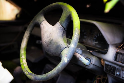 朽ちた車のハンドル、変色した緑色に浮かぶサビと汚れ