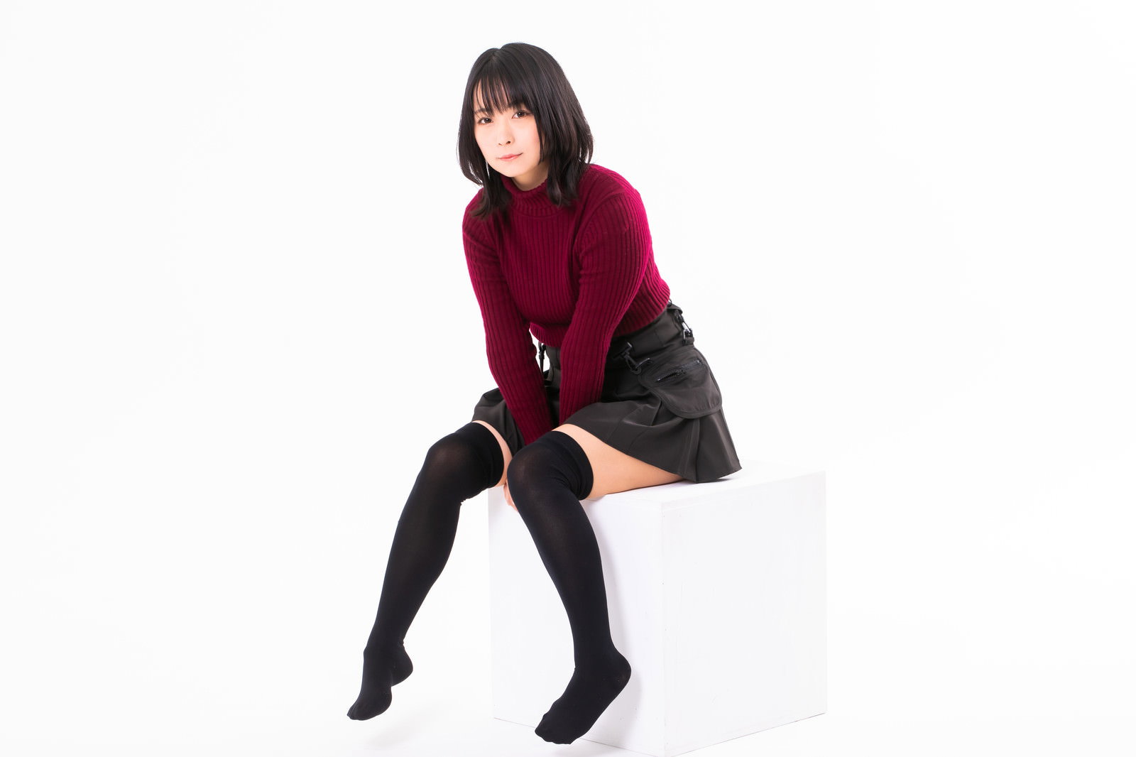黒いハイソックスを合わせた女の子座りをする女性が白い台座に座っている［モデル：にゃるる］