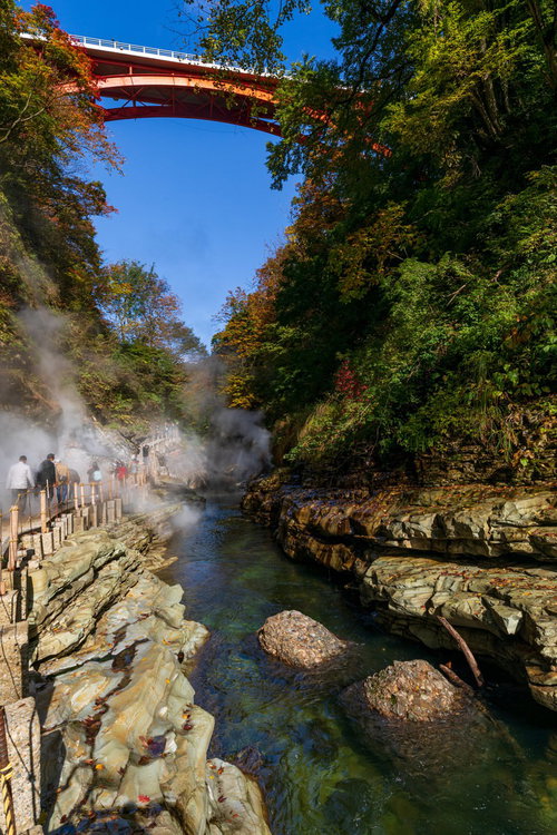 小安峡の渓谷に立ち上る湯けむりと赤い橋の秋景色