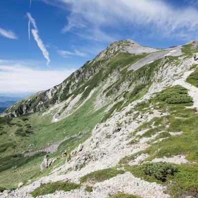 青空を指す笠ヶ岳の登山道を歩む登山者たちの写真