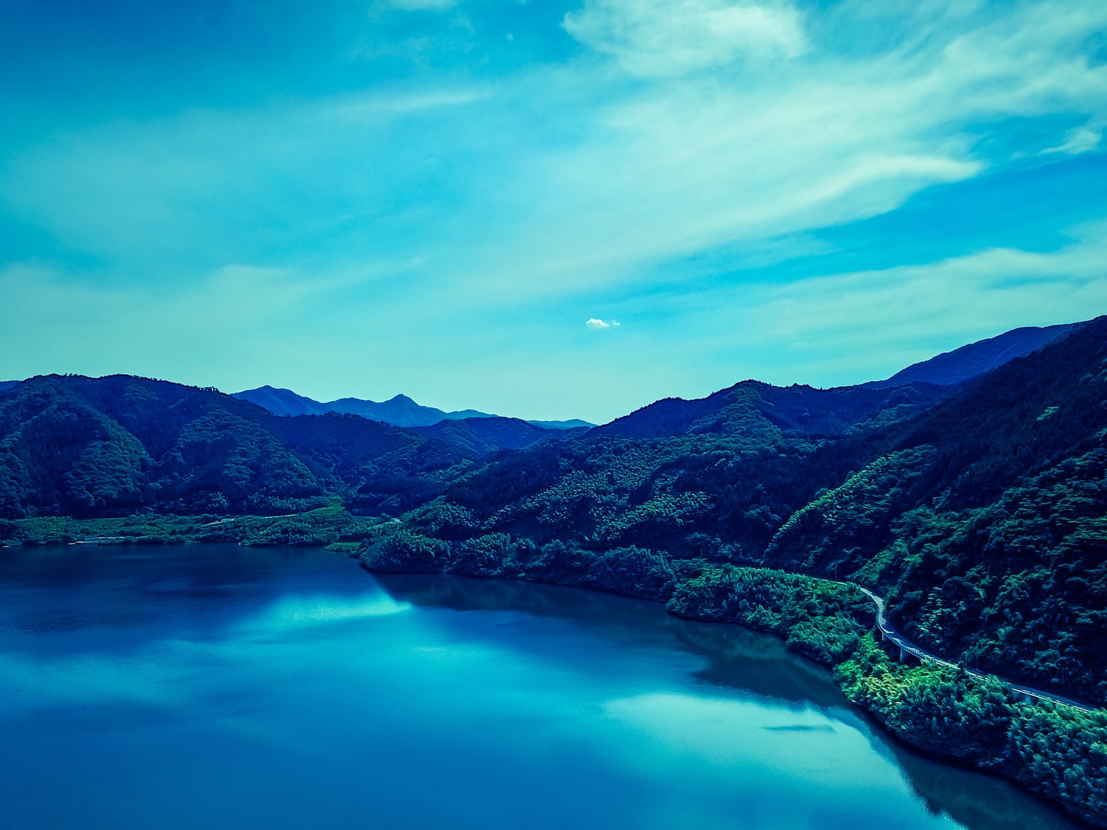 奥津湖を空撮した写真。青い湖面と周囲の山々、青空が広がる自然風景