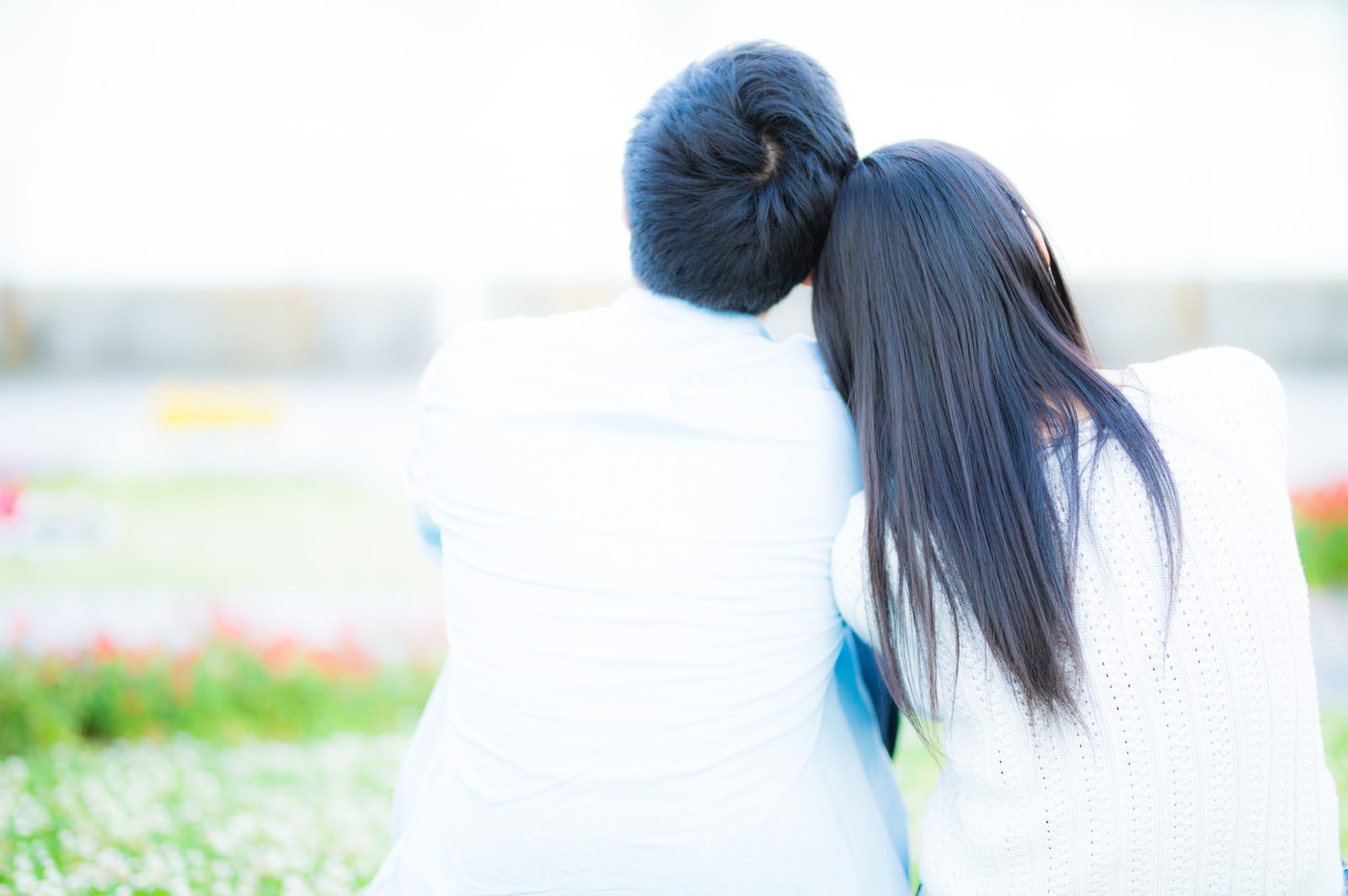 屋外で肩を寄せ合って座っている男女の後ろ姿