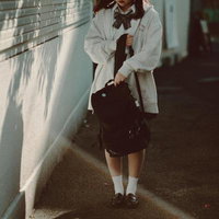 制服とリュックが描く午後の通学路、白い壁沿いを歩く女子高生の写真