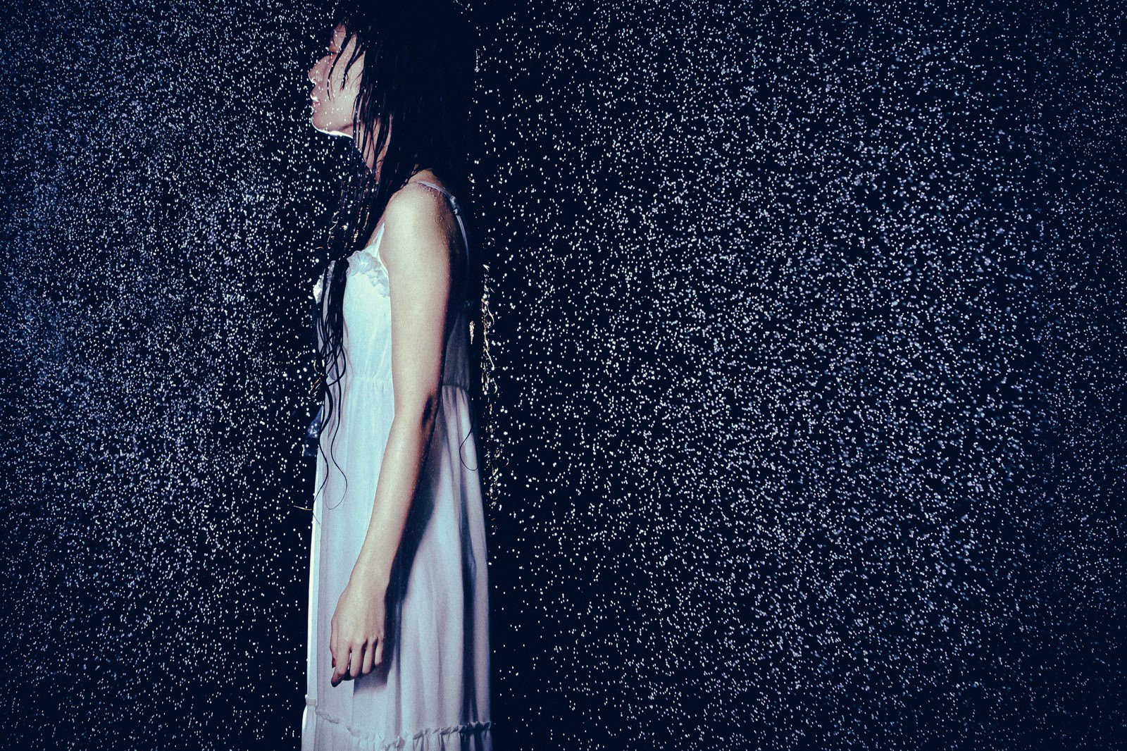 大雨の中で横を向く白いワンピース姿の女性