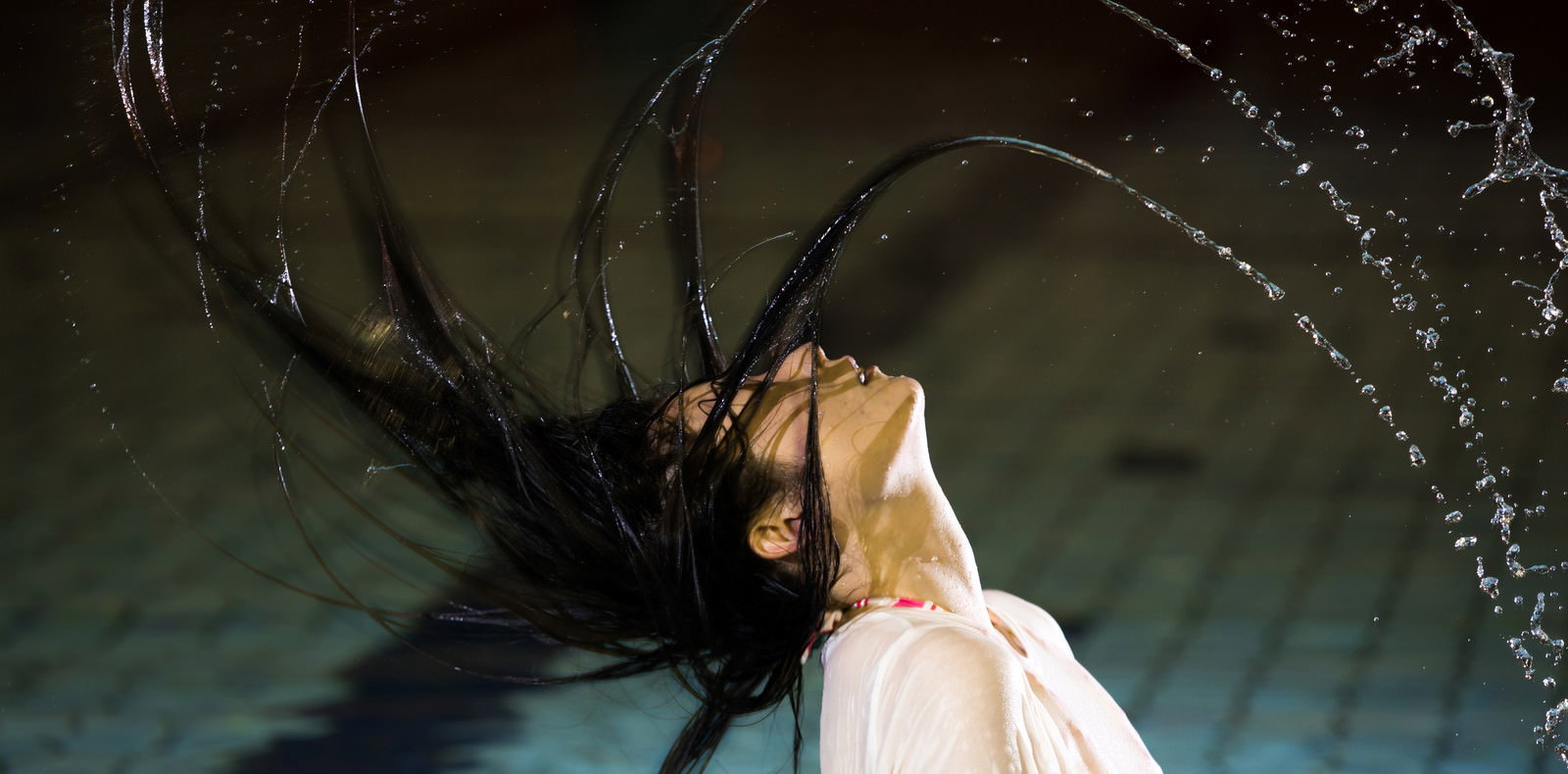 プールで髪を振り上げる女性と飛び散る水しぶき［モデル：たけべともこ］