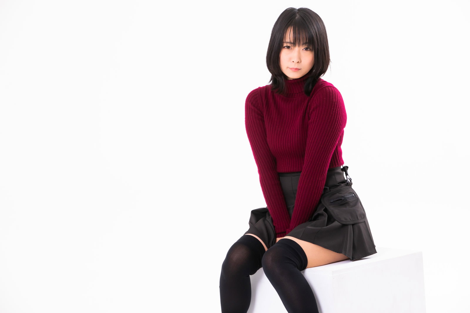 ボルドー色のニットにグレーのスカートを着て座り込む女性［モデル：にゃるる］