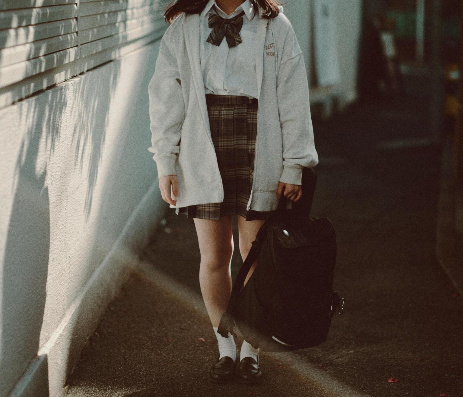 制服を着た女性がリュックを手に持ち通学路を歩く