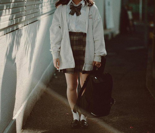 リュックを手に持つ制服姿の女性が歩む通学路での一瞬