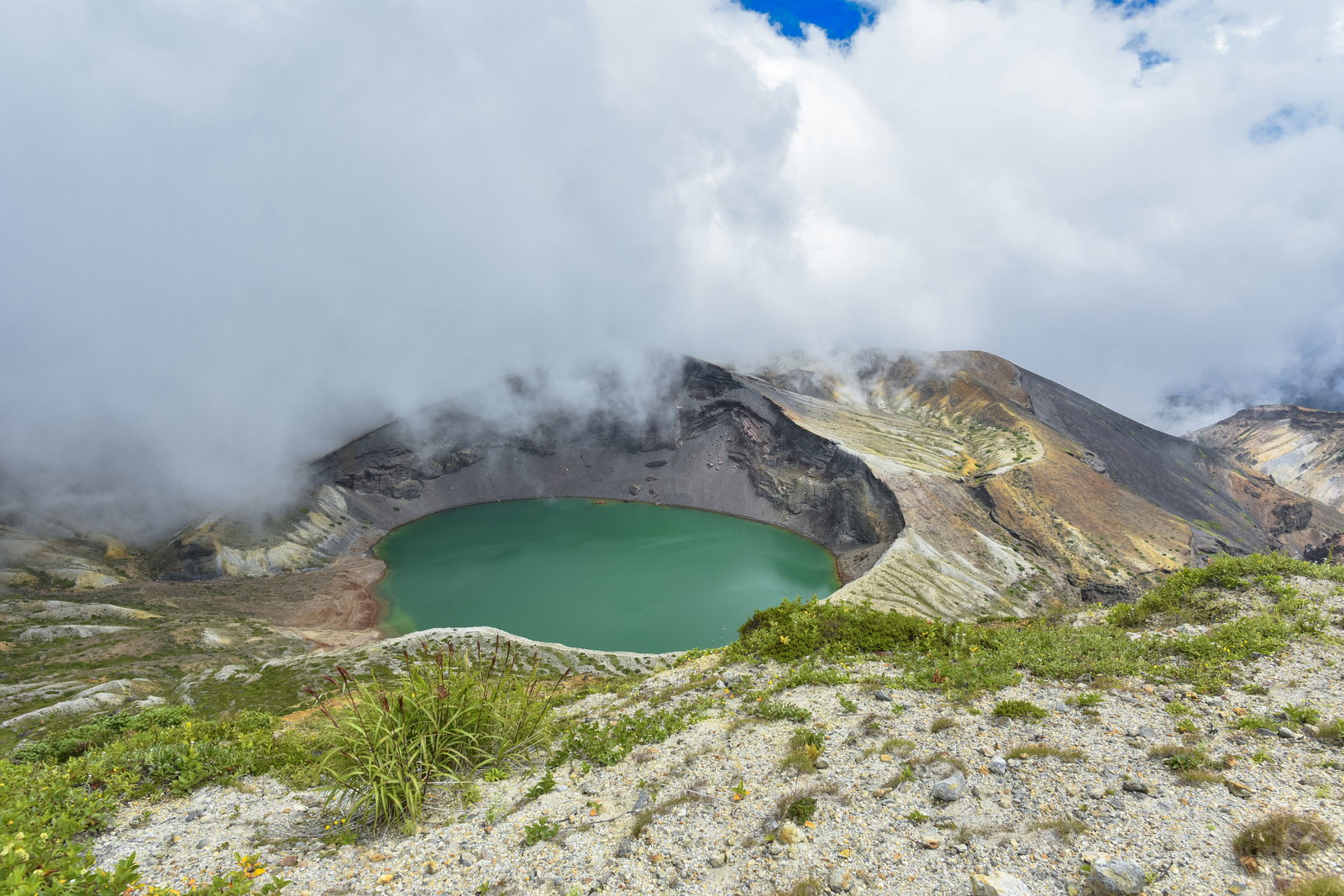 エメラルドグリーンの蔵王山御釜（五色沼）と白い雲が浮かぶ山岳風景