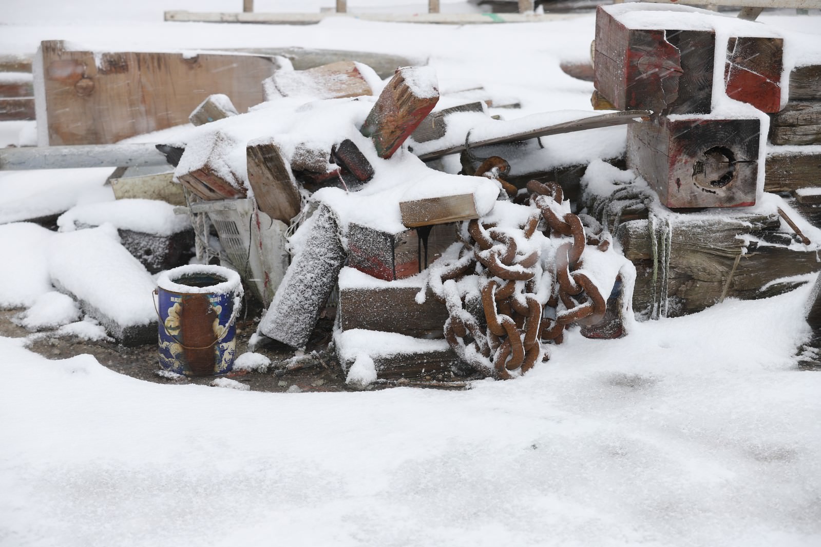 雪に埋もれた錆びた鎖と木材などの廃材が積もった雪の中に見える