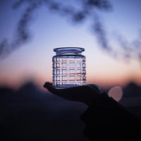 夕焼けの空に透ける格子模様のガラス瓶を手のひらに乗せたの写真