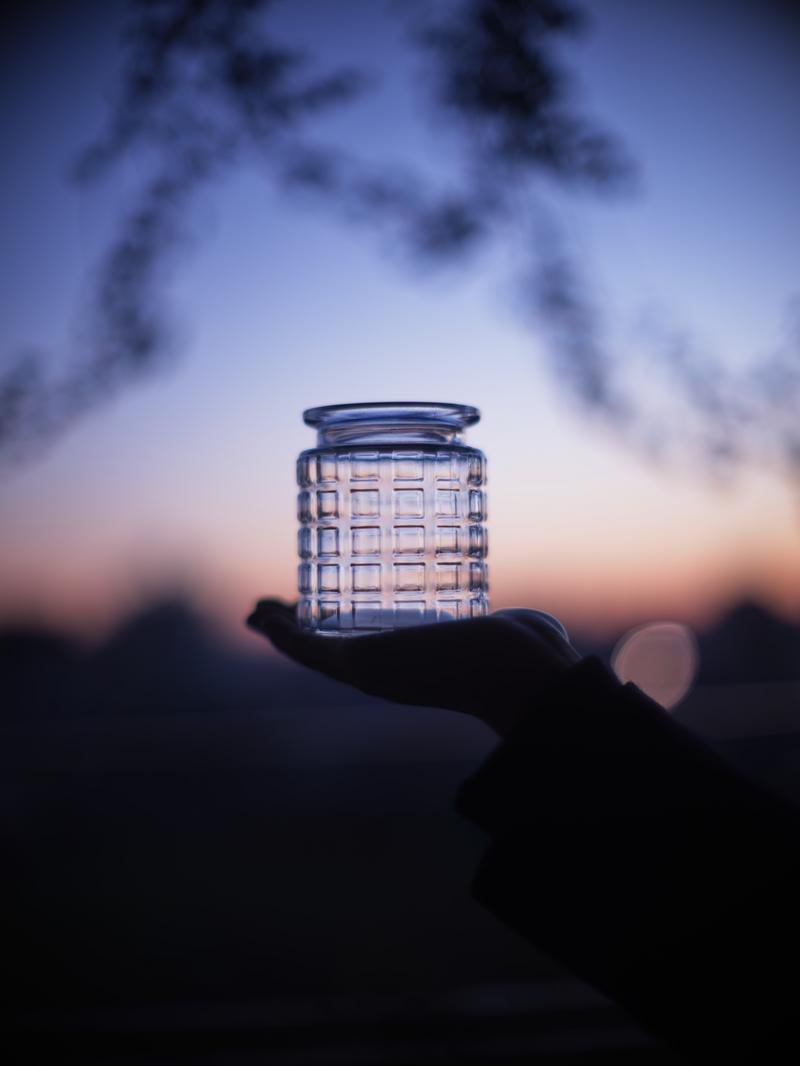 夕焼けの空を背景に、手のひらに乗った格子模様のガラス瓶のシルエット写真