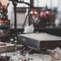 散らかった魔法使いの机に並ぶ古書と結晶とハーブの写真