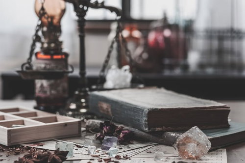 散らかった魔法使いの机に並ぶ古書と結晶とハーブ