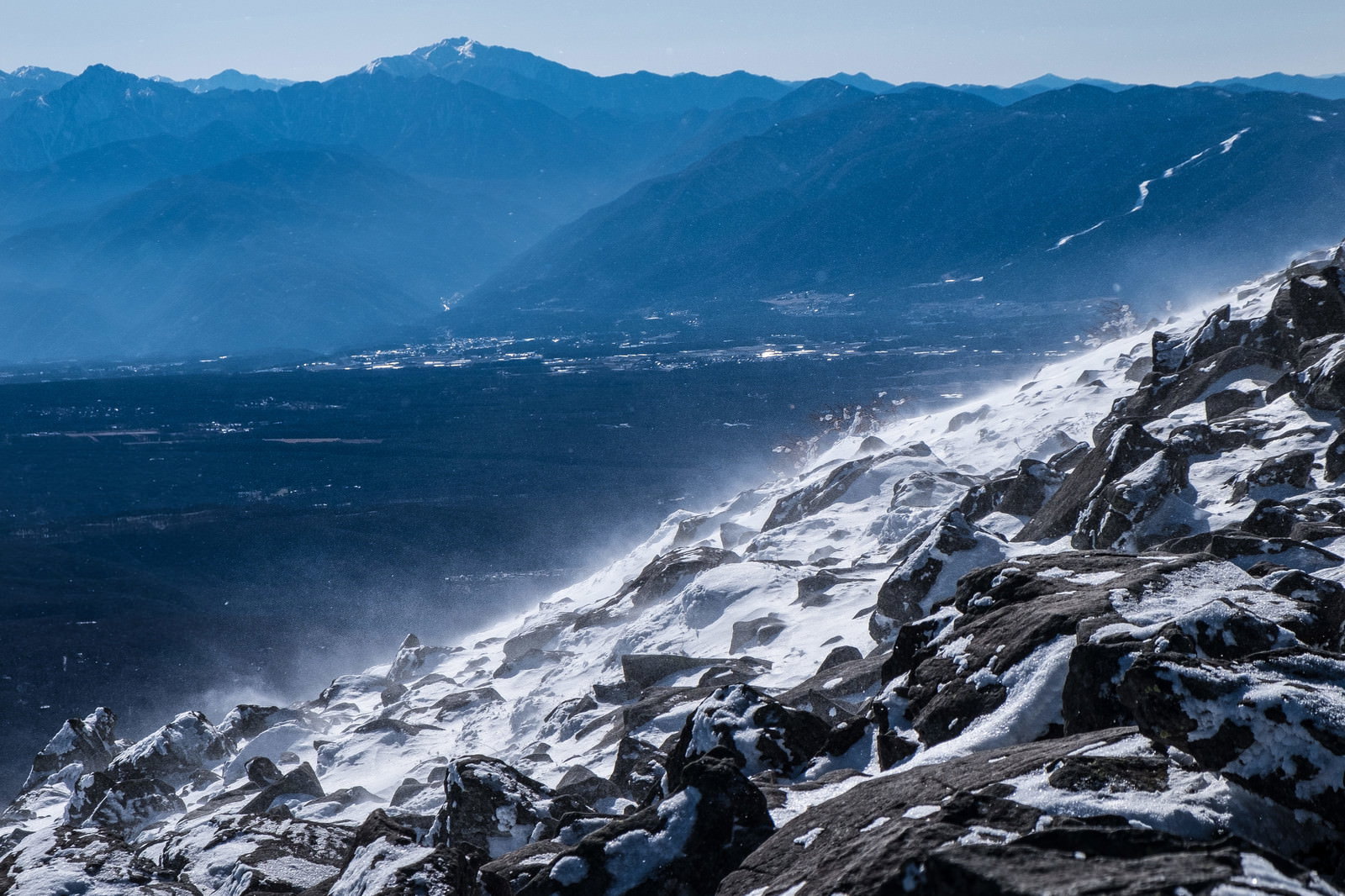 蓼科山の雪に覆われた岩場から望む青空と連なる山脈の風景
