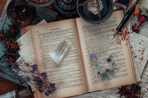 散らかった魔女の机に広げられた古書と魔法の道具