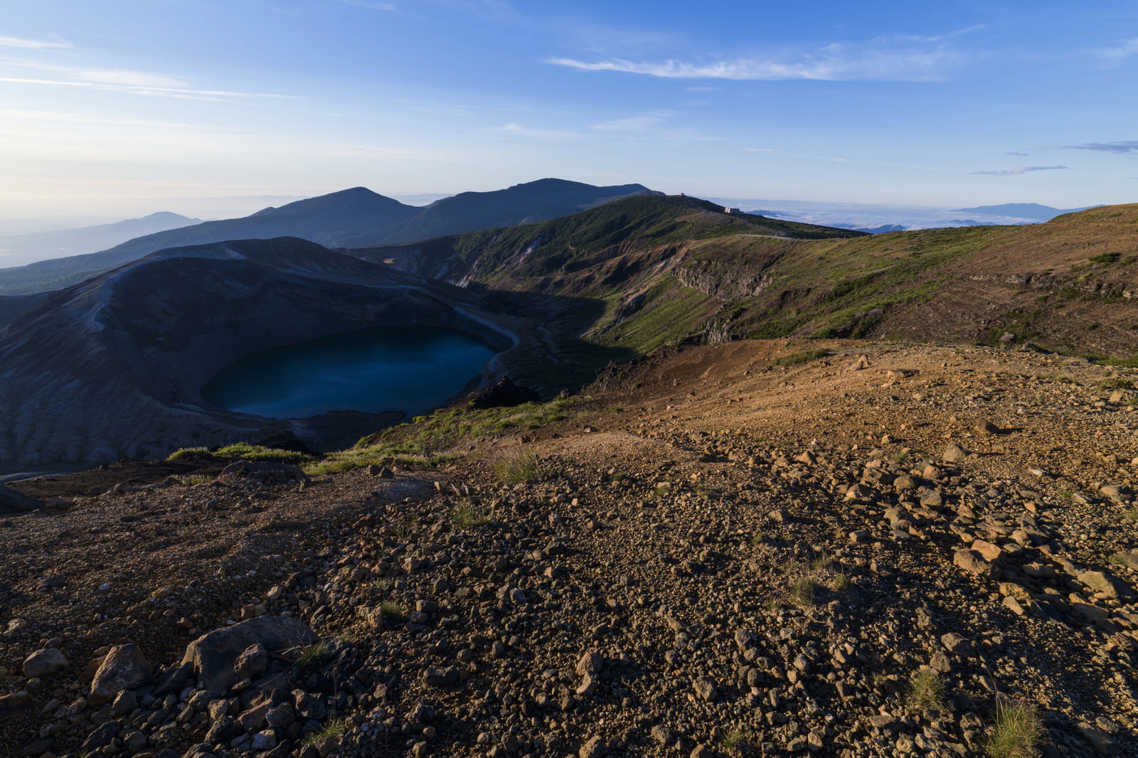 午前の陽光で日陰になった蔵王山の火山口湖・御釜と周囲の山稜