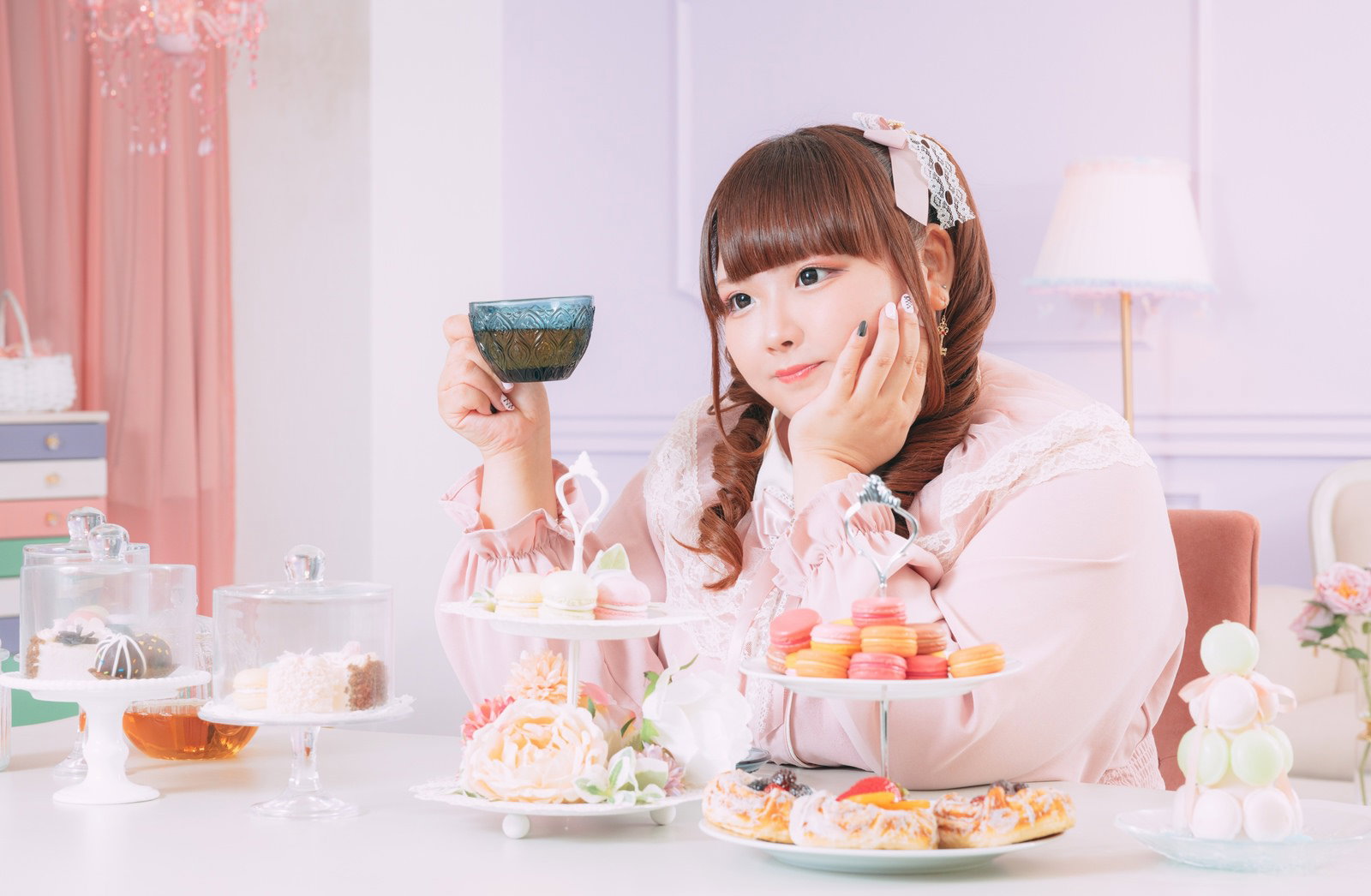 ピンク色の洋服を着た女性がお菓子に囲まれてティータイムを楽しむ様子［モデル：あづき］