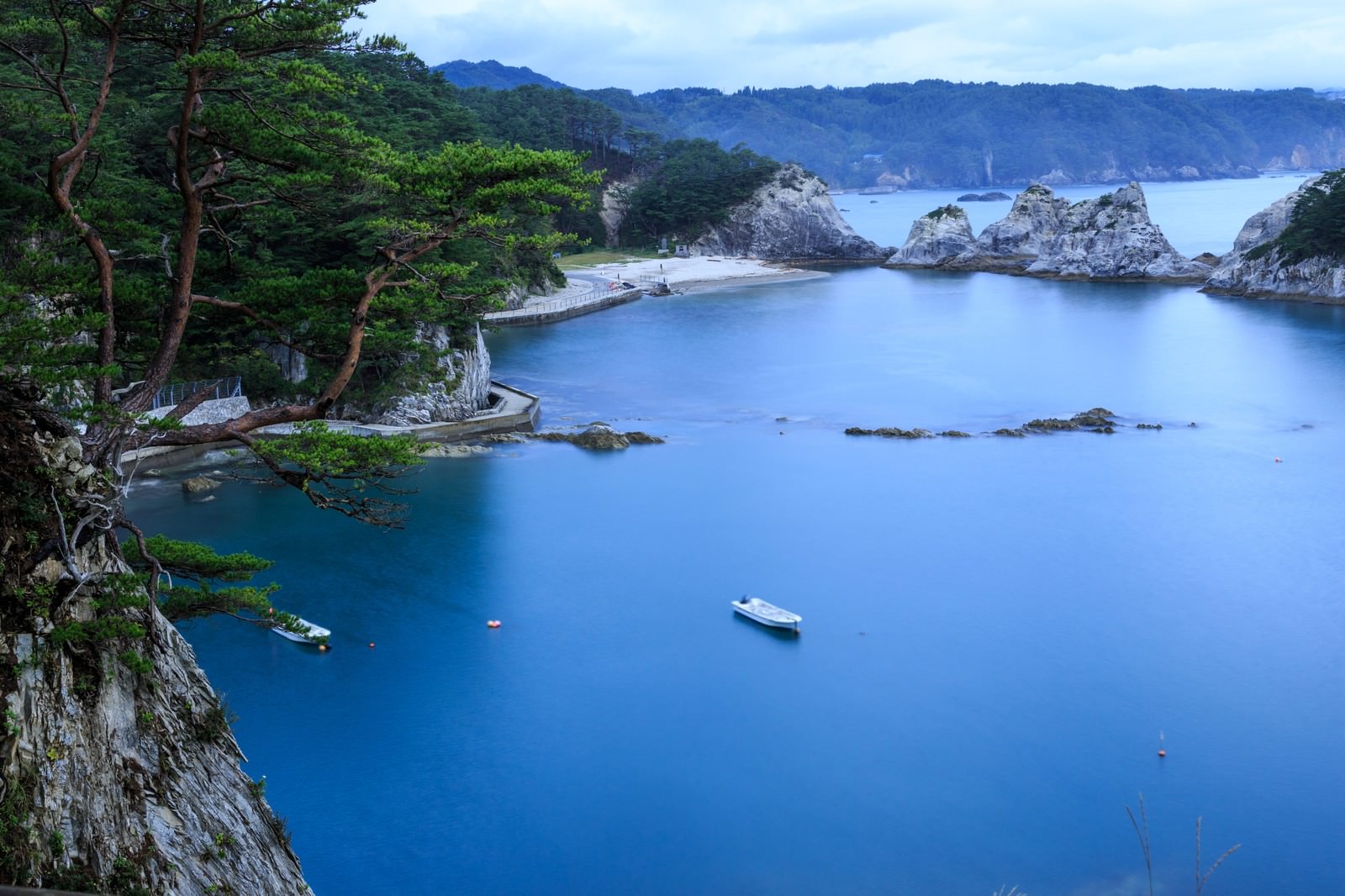 浄土ヶ浜の青い海に白い岩礁が点在し、小さなボートが浮かぶ風景