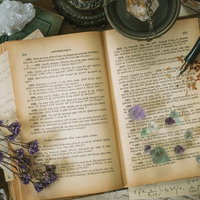 魔女の机に散らばる古書とクリスタル、乾燥ハーブの写真