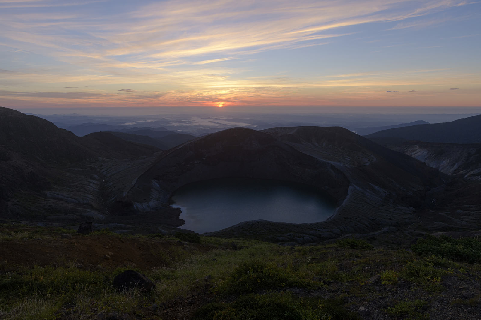 夜明けの空の下で静かに佇む蔵王山の火山口湖御釜と周囲の山々