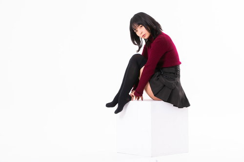 白い箱に座ってカメラを見つめる黒髪の女性の写真