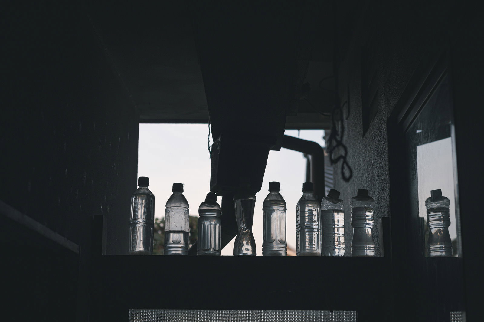 窓際に並んだ複数のペットボトルが逆光でシルエットになっている