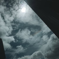 ビルの隙間から見上げる曇り空と太陽の都市風景の写真