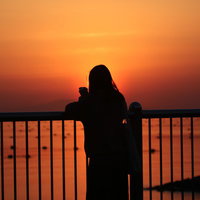 夕暮れの海岸で柵に寄りかかる女性のシルエットの写真
