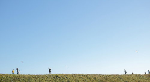 河川敷の芝生で子どもたちと凧あげをする家族