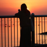 夕焼けに染まる海を眺める女性のシルエットの写真