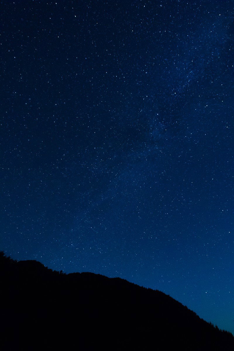 濃紺の夜空に星が散りばめられ、手前に山のシルエットが見える星空の風景