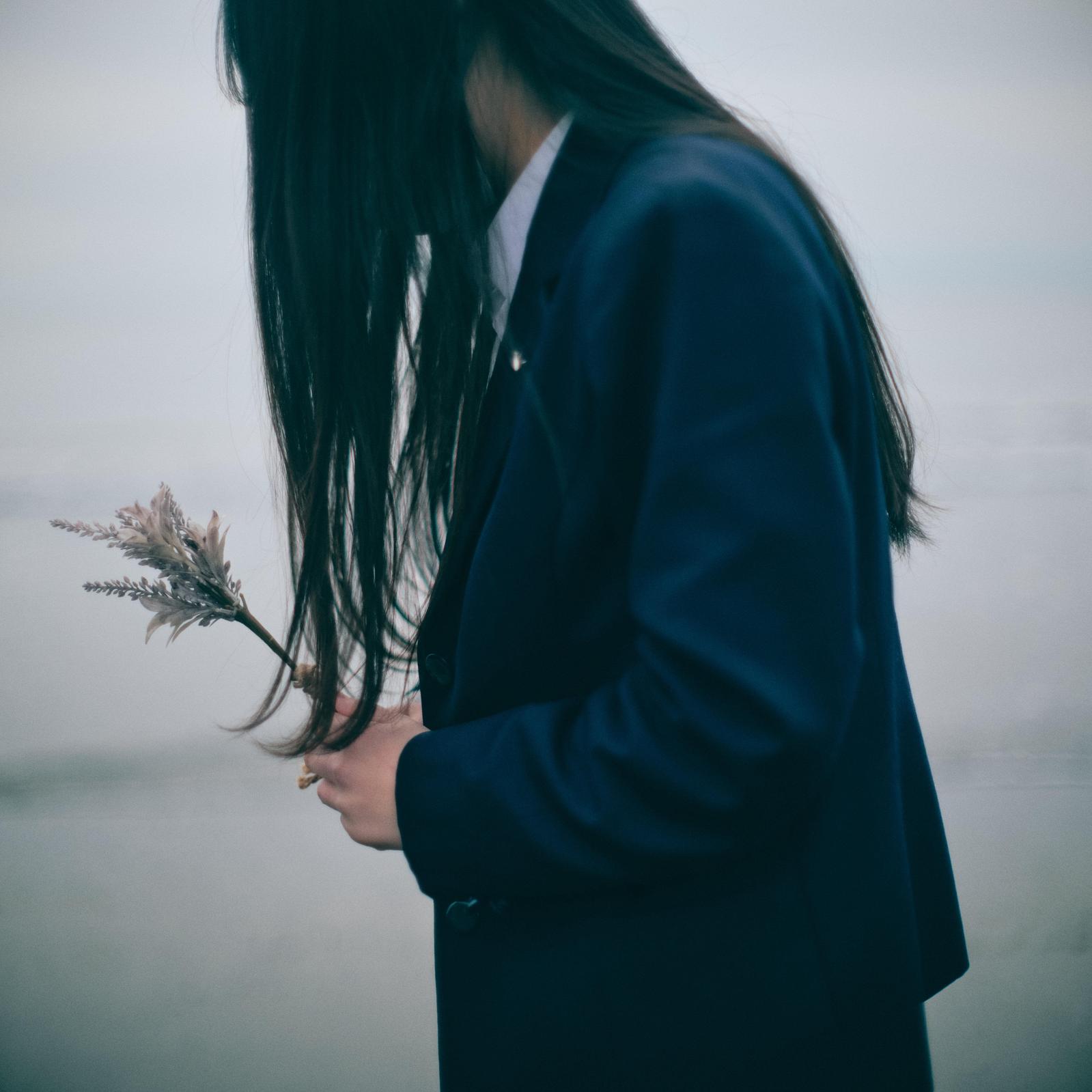 制服姿の女子高生がドライフラワーの束を持ち、黒髪で顔を隠しながら俯いている