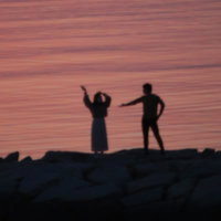 夕焼けの海岸ではしゃぐ恋人達のシルエットの写真